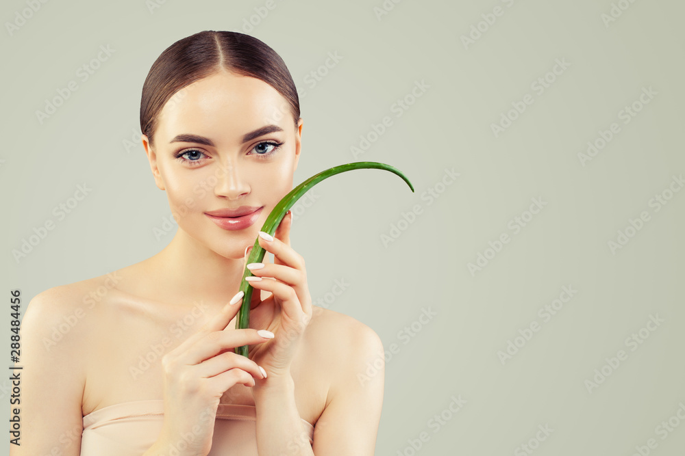 Beautiful young woman with clear skin holding green aloe vera leaf. Skincare and facial treatment concept Beautiful young woman with clear skin holding green aloe vera leaf. Skincare and facial treatment concept
