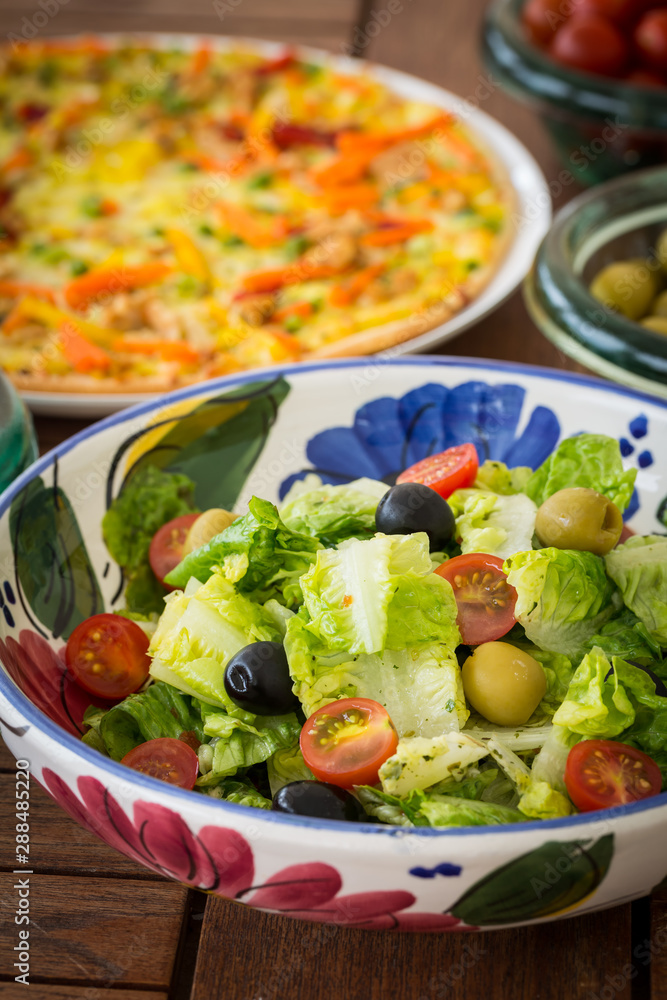 Small lettuce salad with pizza in background Small lettuce salad with pizza in background