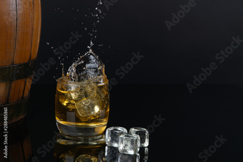 Glass of whiskey with splash, on a black background. old barrel. ice