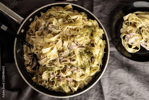 Italian fresh fettuccine pasta with Mushroom and greens in a pan on grey background. top view