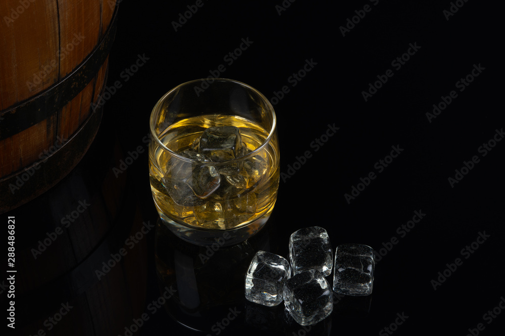 Whiskey with ice in glass on black background. old oak barrel Whiskey with ice in glass on black background. old oak barrel