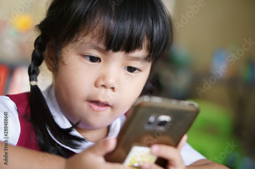 Asian child cute or kid girl student wear school uniform looking smartphone for communication or cartoon and vdo clip with playing game very concentrate which causes ADHD or Hyperactive on pre school