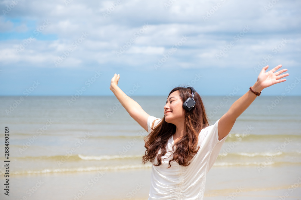 A beautiful asian woman opening arms while enjoy listening to music with headphone by the sea A beautiful asian woman opening arms while enjoy listening to music with headphone by the sea