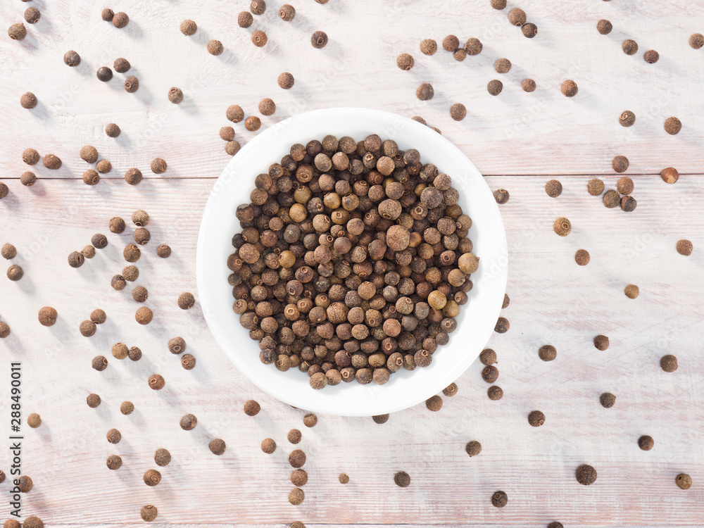 Allspice (Jamaica pepper) in a white cup on a wooden brown background Allspice (Jamaica pepper) in a white cup on a wooden brown background