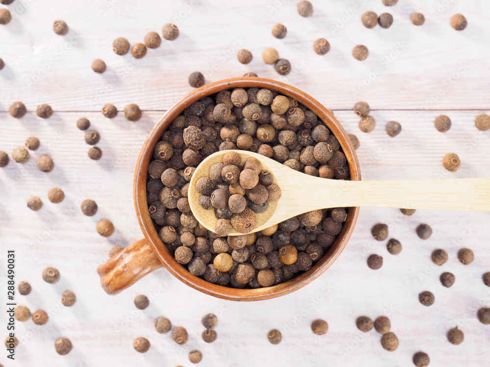 Allspice (Jamaica pepper) in a clay cup and wooden spoon on a brown wooden background Allspice (Jamaica pepper) in a clay cup and wooden spoon on a brown wooden background