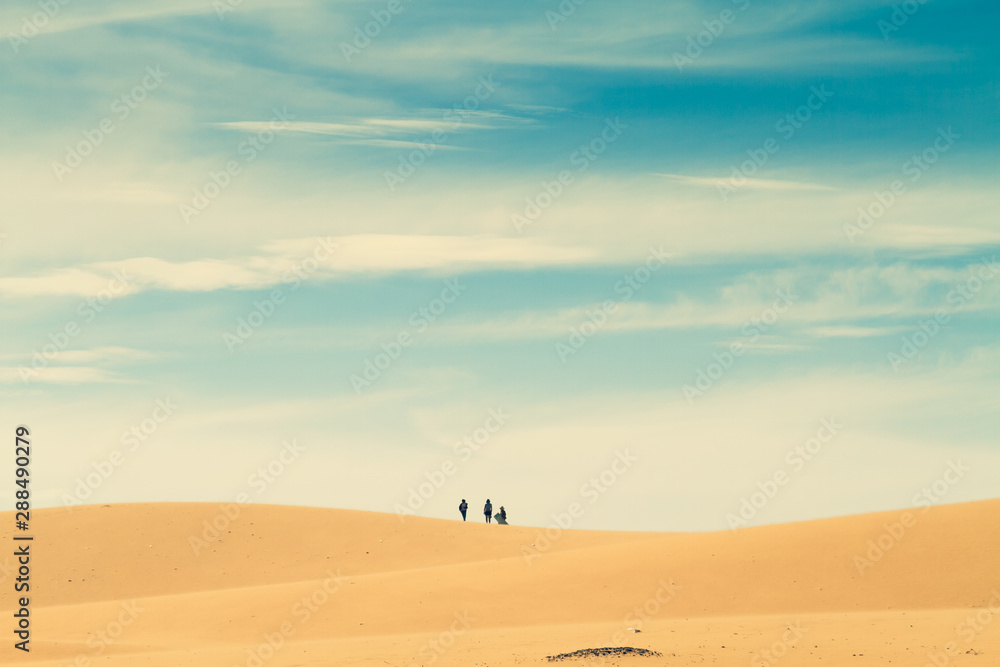 Group people in the distance walk on top of a hill in the desert.