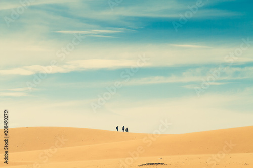 Group people in the distance walk on top of a hill in the desert.