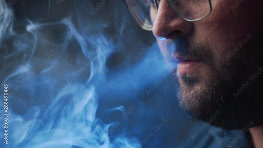 Man smokes new Vape Pod System, inhales and exhales vapor of electronic cigarette, vaping concept Man smokes new Vape Pod System, inhales and exhales vapor of electronic cigarette, vaping concept