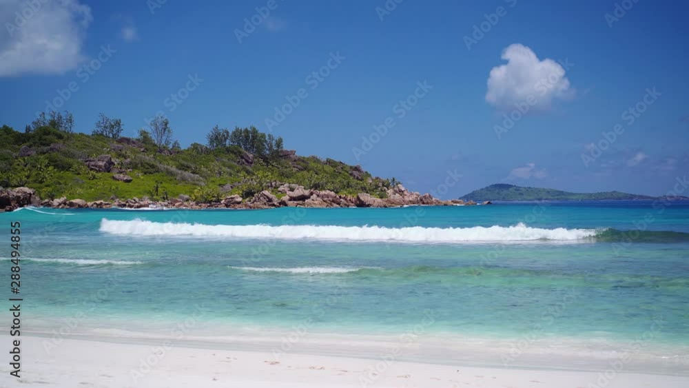 Anse Coco beach on La Digue, Seychelles. Calm ocean waves rolling to white sand tropical coast and blue sky. Praslin Island in background Anse Coco beach on La Digue, Seychelles. Calm ocean waves rolling to white sand tropical coast and blue sky. Praslin Island in background