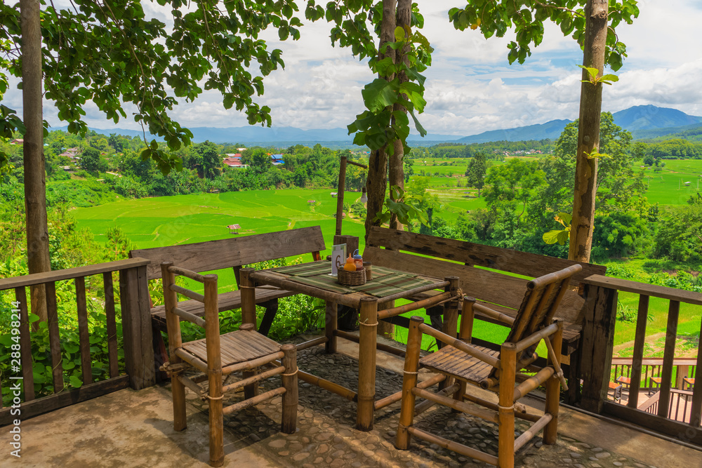Bamboo chair and table over terrace rice green field with mountain and blue sky background