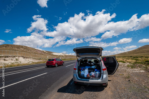 Car - minivan stands on the side of the road with an open trunk, a lot of luggage is visible, summer, mountains, the concept of traveling by car