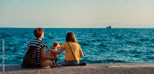 Fototapeta Mother and daughter sitting on the waterfront with dog