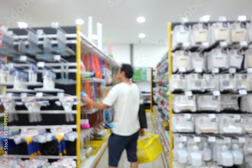 Blurred asian male standing in superstore aisle with a yellow basket and try to choose a craftsman tool from a shelf