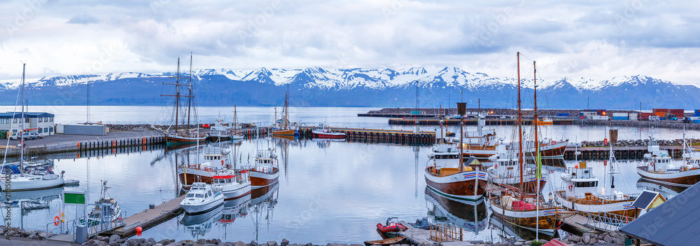 Iceland, Husavic town location. Picturesque panoramic view of northern town Husavik, old harbor with anchored wooden vessels operated for whale watching excursions. Blue hour dusk tranquil scenery.