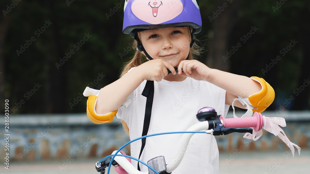 Obraz premium Portrait of little cute caucasian girl puts on a safety bicycle helmet and smiling