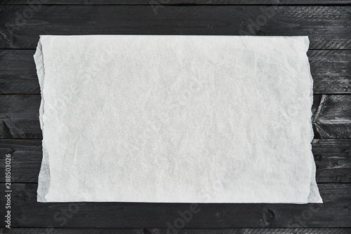 Crumpled piece of white parchment or baking paper on black wooden table. Top view. Copy space for text and design element. photo