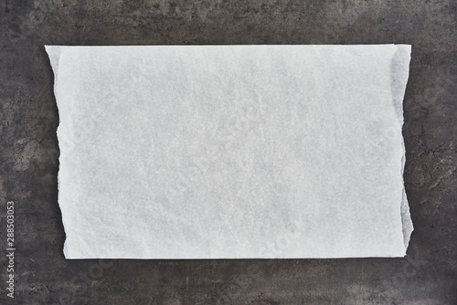 Crumpled piece of white parchment or baking paper on black concrete background. Top view. Copy space for text and design element. photo
