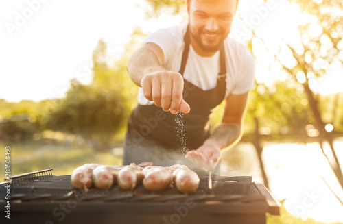 Smiling chef salting sausages on grill photo