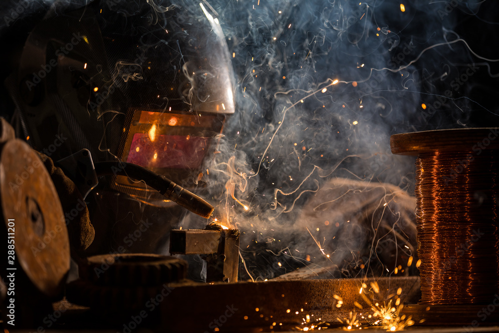 Welder is welding metal part in industrial workshop. - obrazy, fototapety, plakaty 