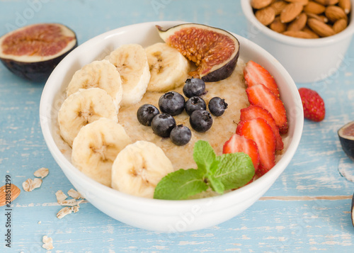 oatmeal with blueberries, strawberries, figs, banana and almonds. Healthy breakfast on a wooden blue background. 