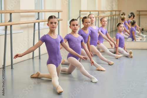 Young ballerinas stretching on the floor. Group of young ballet dancers sitting on the floor and practicing stretching at choreography lesson.
