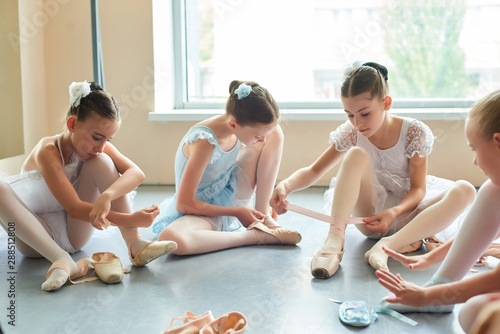 Young ballerinas tying pointe shoes. Four beautiful ballet dancers in dresses sitting on the floor and putting on ballet slippers. Preparation for performance. photo