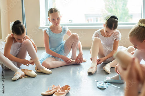 Young ballerina sitting on floor and looking at camera. Group of beautiful young ballerinas putting on ballet shoes. School of ballet dance. photo