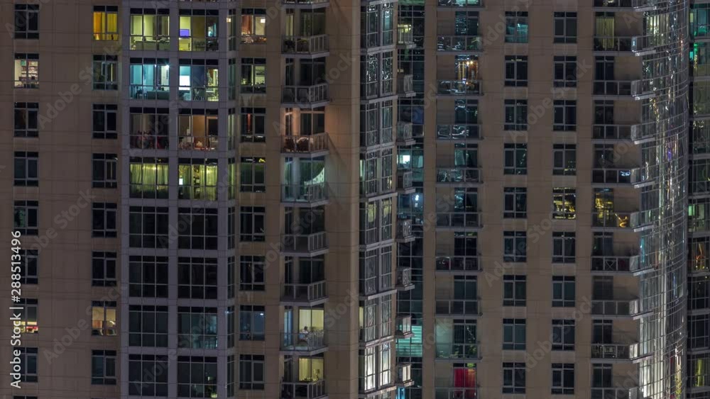 Windows of the multi-storey building with lighting inside and moving people in apartments timelapse. Aerial view of modern residential skyscrapers in Dubai downtown. Pan right Windows of the multi-storey building with lighting inside and moving people in apartments timelapse. Aerial view of modern residential skyscrapers in Dubai downtown. Pan right