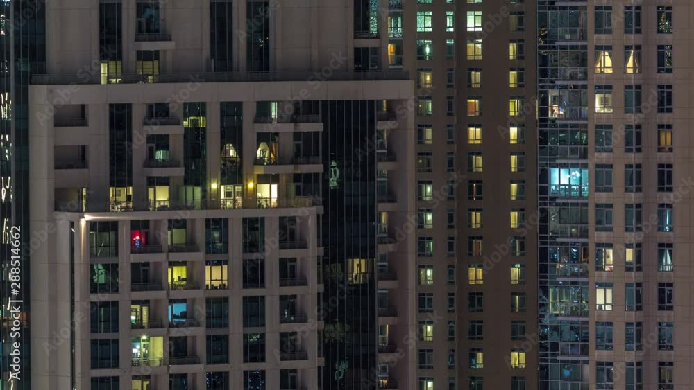Windows of the multi-storey building with lighting inside and moving people in apartments timelapse. Aerial view of modern residential skyscrapers in Dubai downtown. Pan left Windows of the multi-storey building with lighting inside and moving people in apartments timelapse. Aerial view of modern residential skyscrapers in Dubai downtown. Pan left