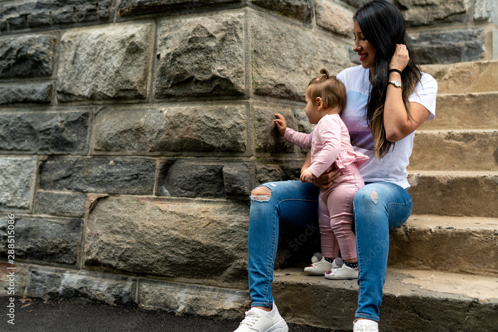 mother sitting on stone steps with daughter touching stone wall
