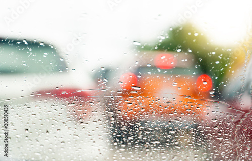 Abstract background of blurred image cars on the road during the rainy time. The view through the glass of the car with rain drops.
