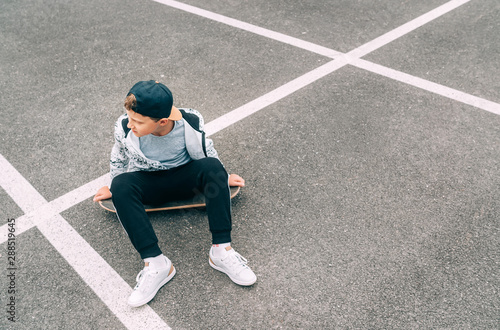 Teenager skateboarder boy with a skateboard sitting on asphalt playground and resting after he made tricks. Youth generation Freetime spending concept image.