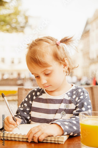 Humorous portrait of little female artist designer draws a pencil sketch on notebook (creativity, art, training concept)