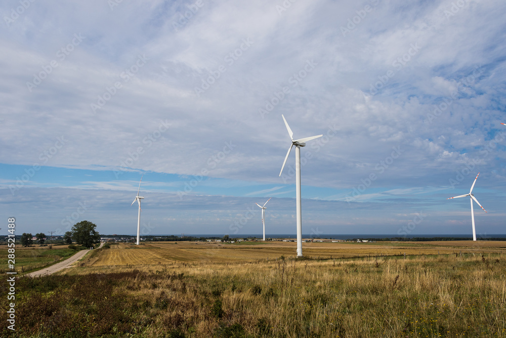 Landscape with mills of the wind power plant on the field under the blue cloudy sky on a sunny day.