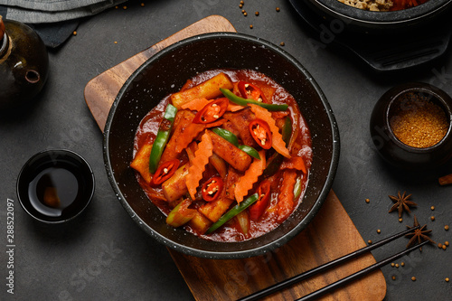 Korean Food Style : Top view of Hot and spicy Stir-fried rice cake ( Tteokbokki ) put in the black bowl or dish and placed on a wooden tray