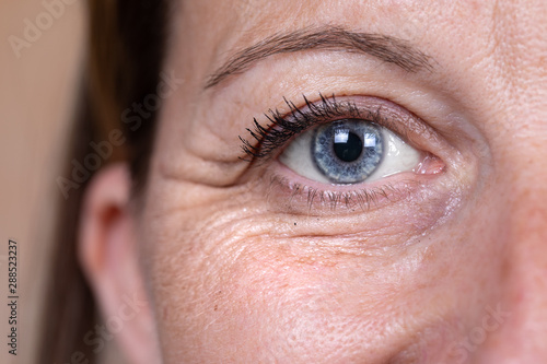 A close up and front view on the blue eye of a mature caucasian woman in her forties, showing heavy wrinkles (crow's feet) in the corner and below the eye, with copy-space.