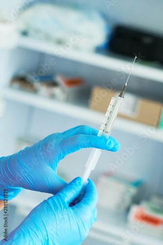 Close-up hands of young woman doctor anesthesiologist dressed in pink gown, blue gloves prepares solution for anesthesia in the operating room before the surgery.