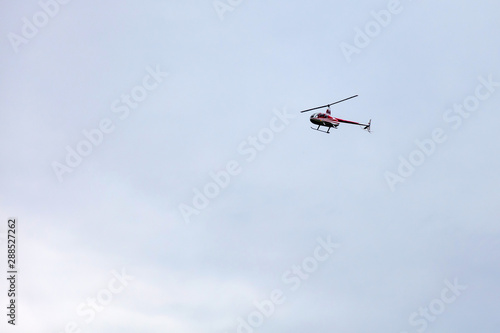 A red pleasure helicopter flies in the sky during a sightseeing walk against a gray sky. Air Transport.