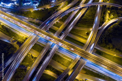 Aerial view of illuminated road interchange or highway intersection with busy urban traffic speeding on the road at night. Junction network of transportation taken by drone.