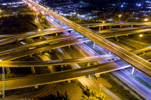 Aerial view of illuminated road interchange or highway intersection with busy urban traffic speeding on the road at night. Junction network of transportation taken by drone.