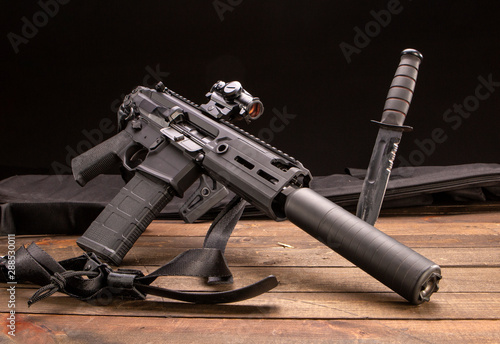 Studio shot of a semi-automatic rifle with a silencer and a Ka-Bar. photo