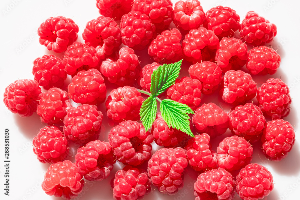 Fresh red raspberries are scattered on a white surface. A lot of berries and one leaf. View from above Fresh red raspberries are scattered on a white surface. A lot of berries and one leaf. View from above