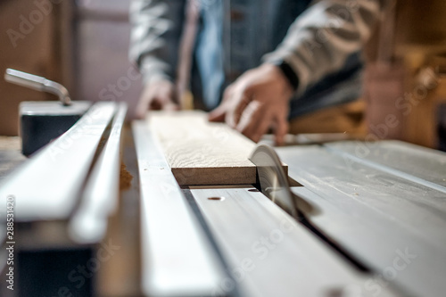 Caucasian man making wooden parts for custom furniture on machine tool called thickness planer in carpentry. Producing lumber concept photo
