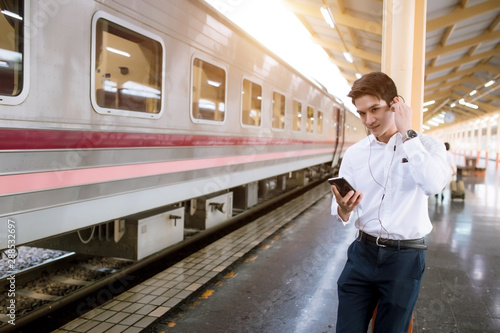 Portrait Man listening music with his smartphone in train station. Man waiting train at station.