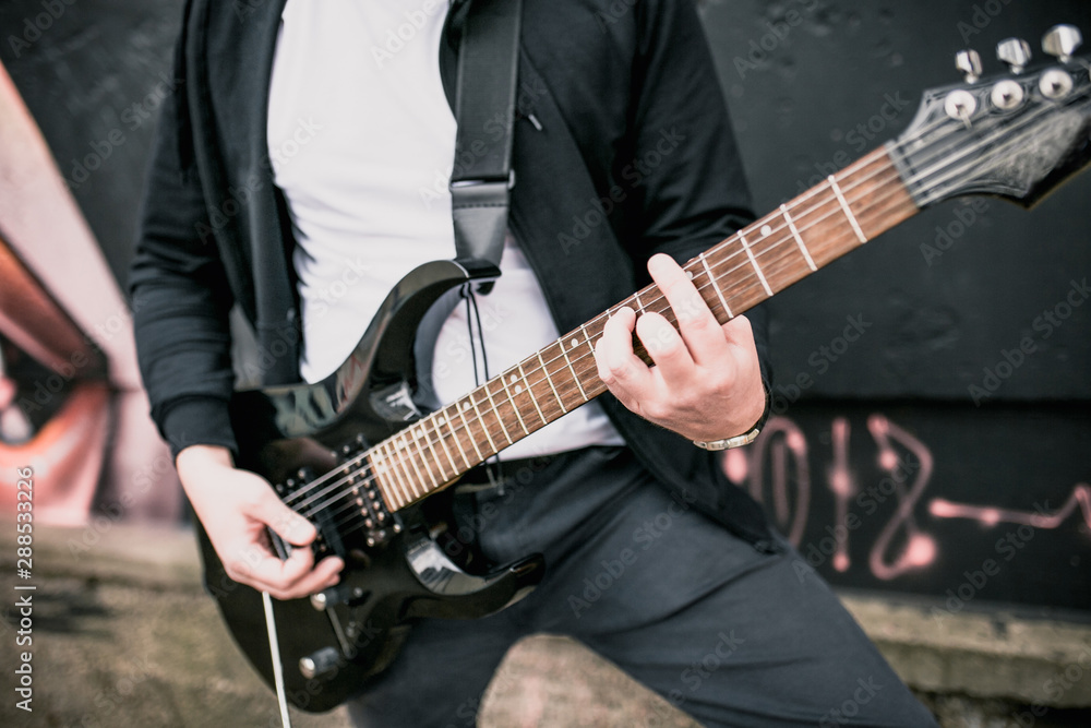 A man plays power chords on a black electric guitar outdoors - hard rock music