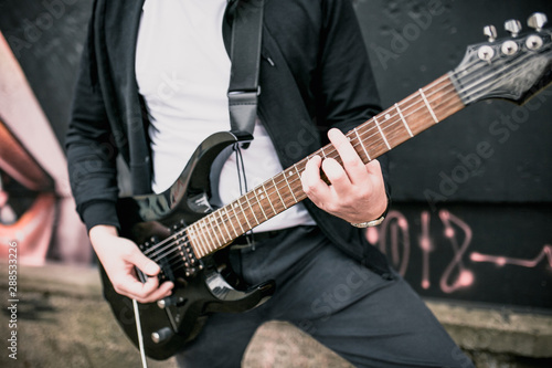A man plays power chords on a black electric guitar outdoors - hard rock music