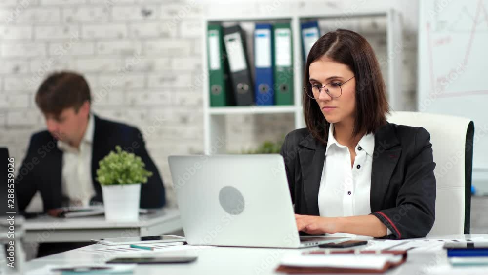 Focused stylish young business woman and man working at modern workplace looking at screen of laptop Focused stylish young business woman and man working at modern workplace looking at screen of laptop
