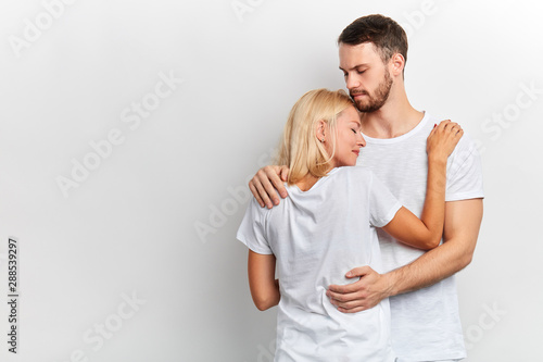 Fotografija Supportive guy hugs and tries to appease his girlfriend who has desperate look, girl has problems, isolated white background, studio shot, copy space