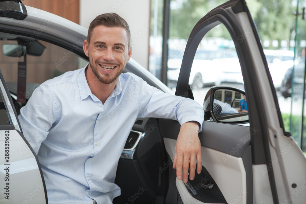 Handsome young man buying a new car at dealership salon Handsome young man buying a new car at dealership salon