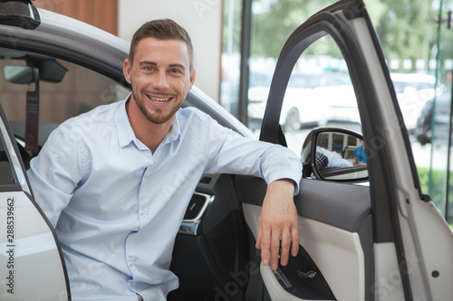 Handsome young man buying a new car at dealership salon